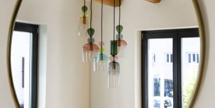 Suspension en verre soufflé multicolore reflétée dans un miroir rond à contour doré, avec poutres apparentes en bois, décoration intérieure sur mesure à Mulhouse par Nadine Rapp