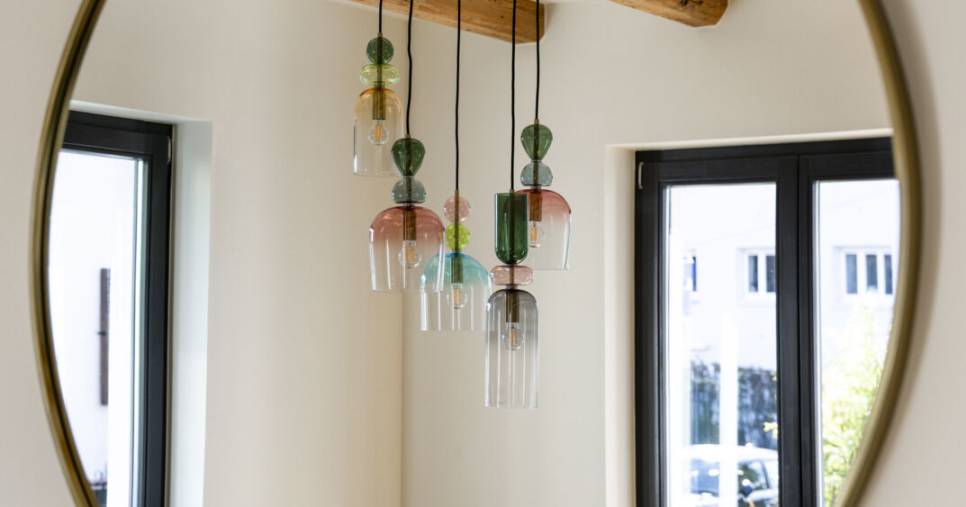 Suspension en verre soufflé multicolore reflétée dans un miroir rond à contour doré, avec poutres apparentes en bois, décoration intérieure sur mesure à Mulhouse par Nadine Rapp